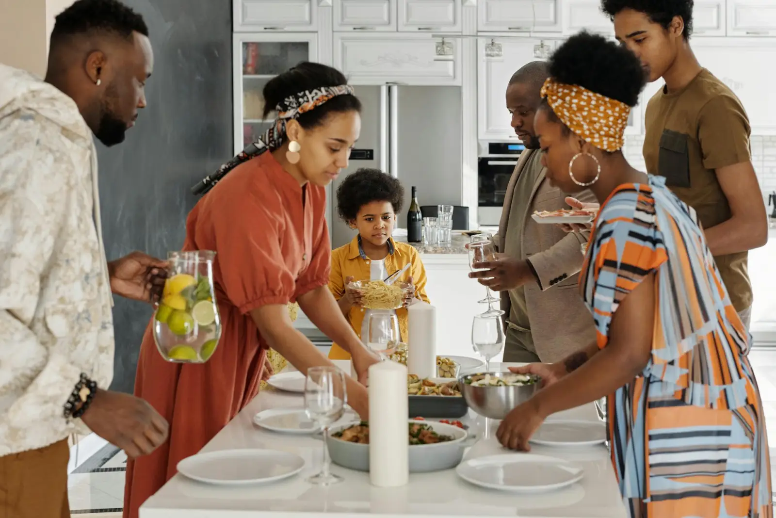 Multi-generational Black family setting the table together in a bright modern kitchen before dinner