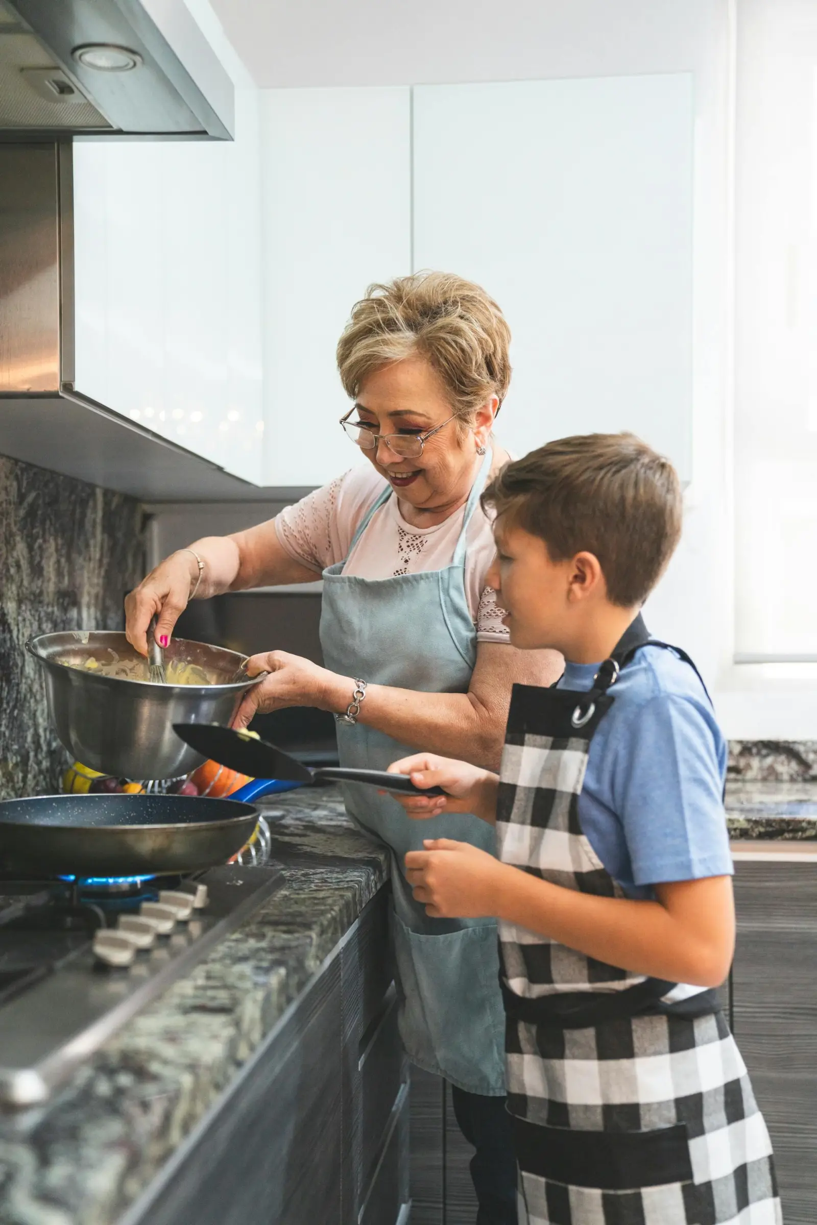 Older Hispanic grandmother and grandchild cooking together in a bright home kitchen